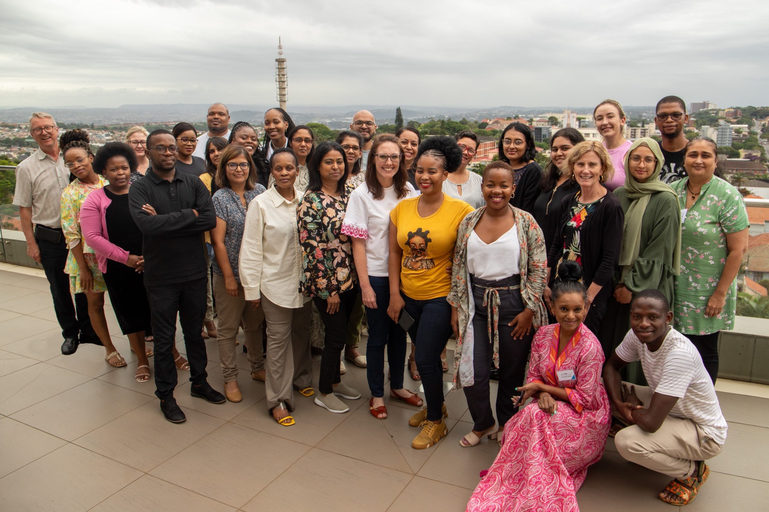 Group photo of course participants and teachers. Picture taked outside with a glimpse of the city in the background.